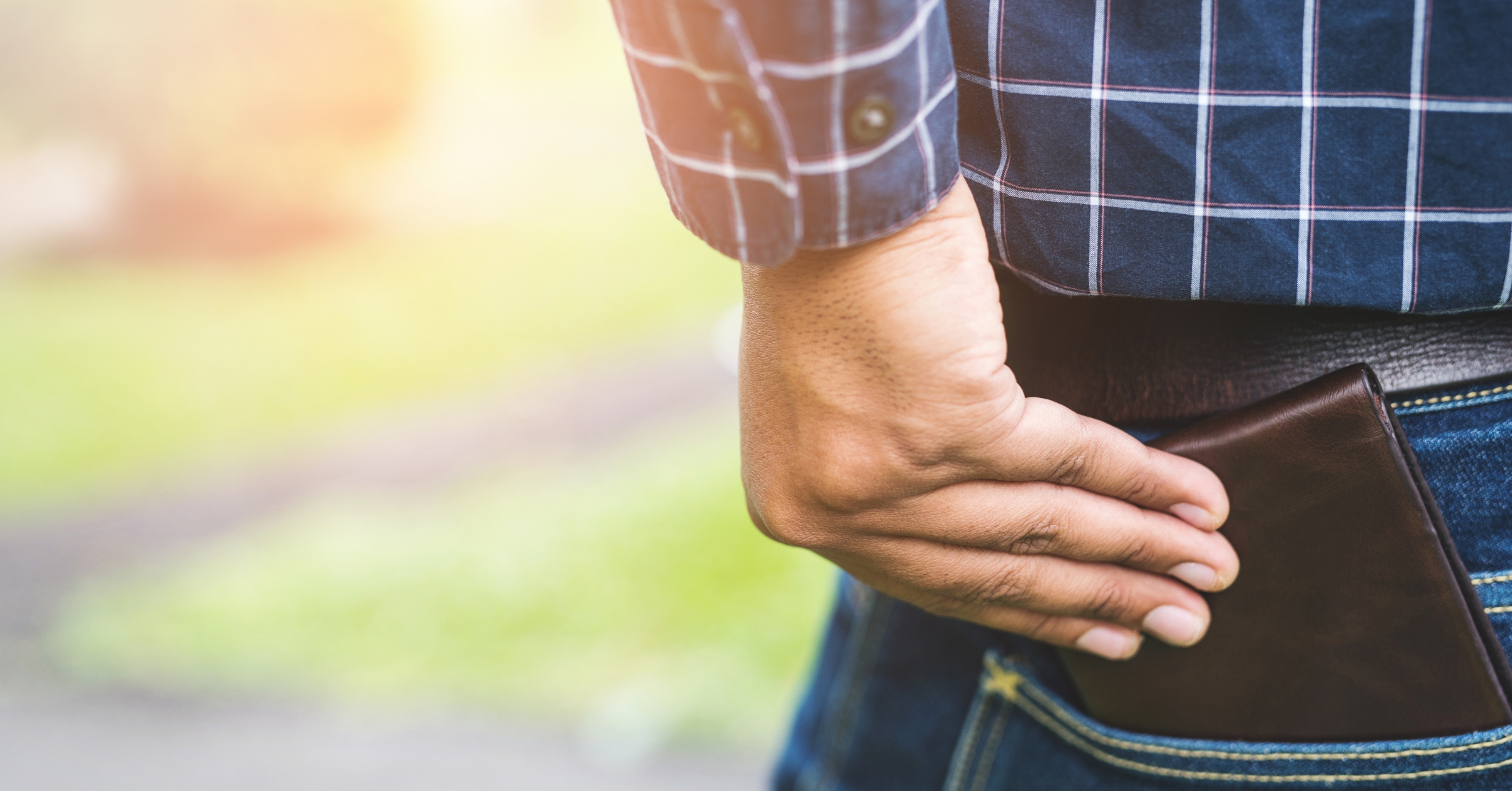 Close-up of a man in casual attire sliding a minimalist wallet into his back pocket. The sleek design of the wallet highlights its compact functionality, perfect for men seeking a blend of style and practicality.