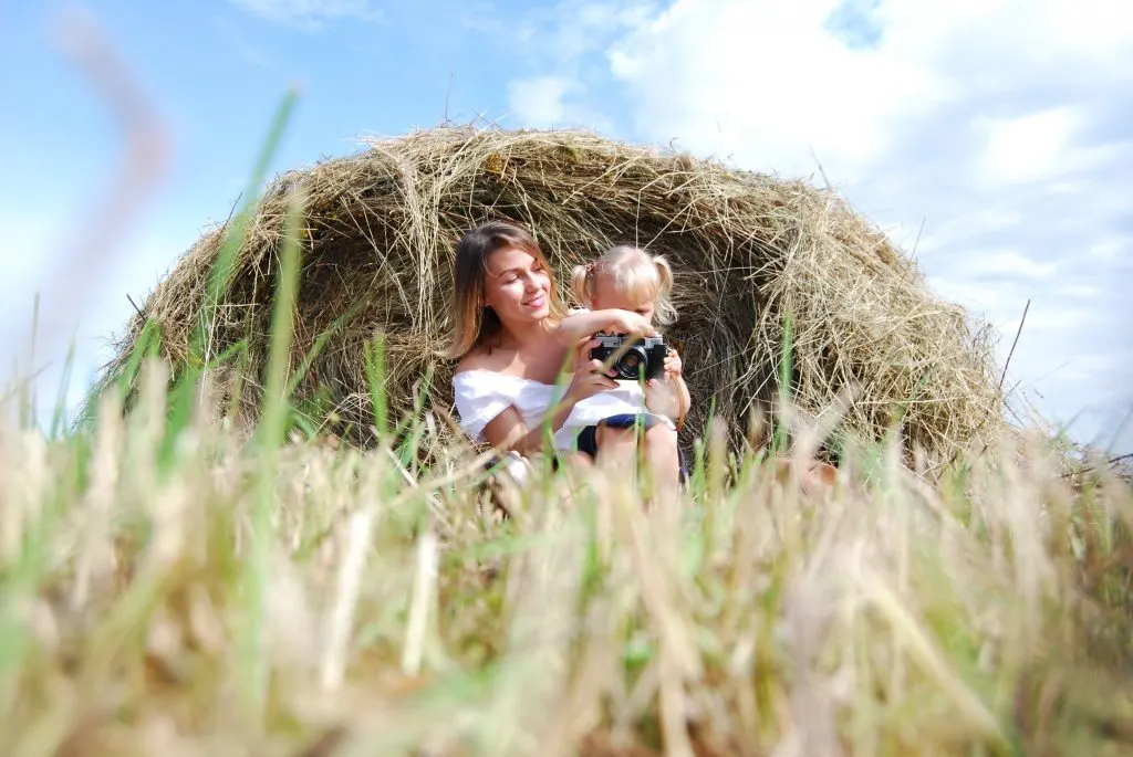 woman in a field with a young girl playing with a camera