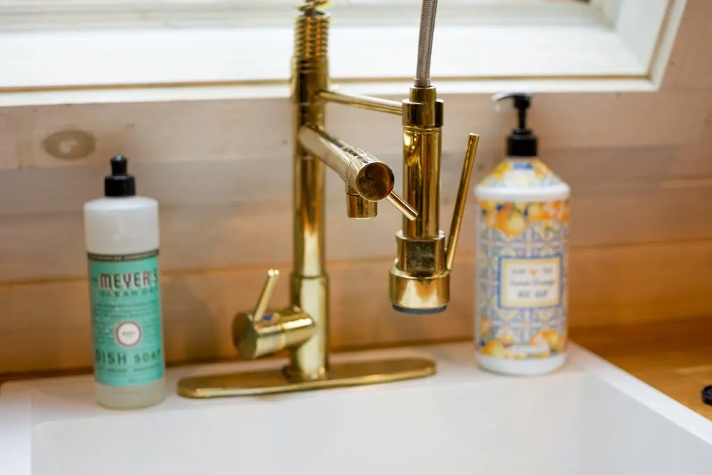 Shiny gold faucet with dish soap and hand soap on the edge of the sink