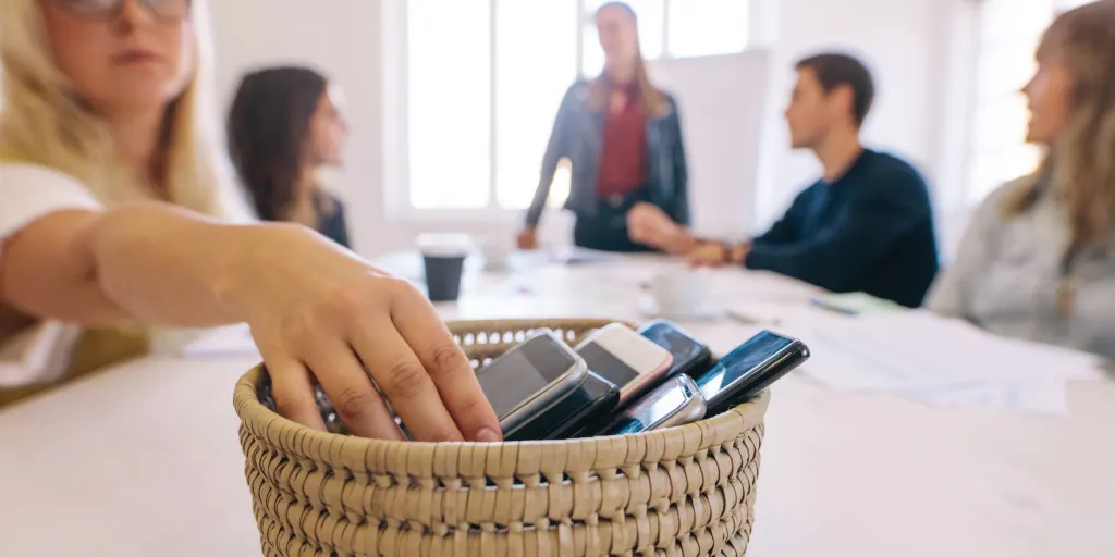 digital decluttering with mindful technology usage by putting phones in a basket during a meeting