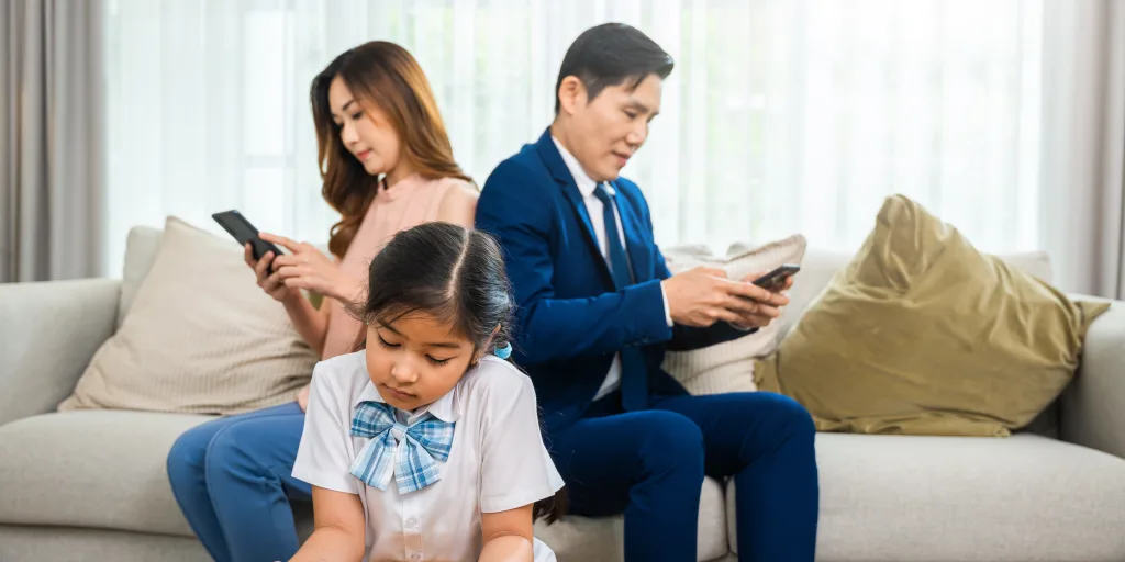 man and woman staring at their phones while little girl plays by herself in front of them. they need digital minimalism.