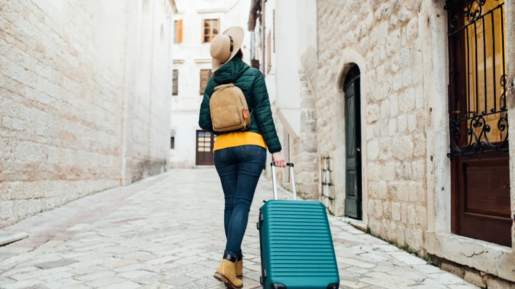 A woman walking down a gravel stone street pulling her luggage.