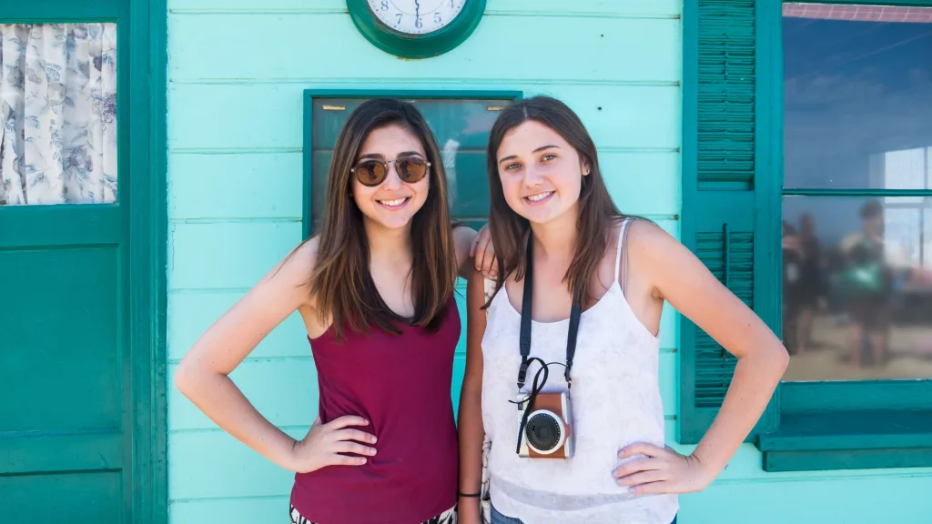 Two teenagers posing in front of a blue beach house. 