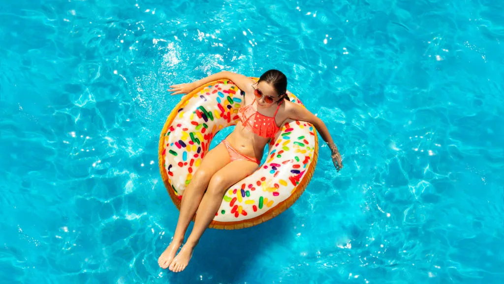 A teenager floating on a flotation donut while at a pool. 