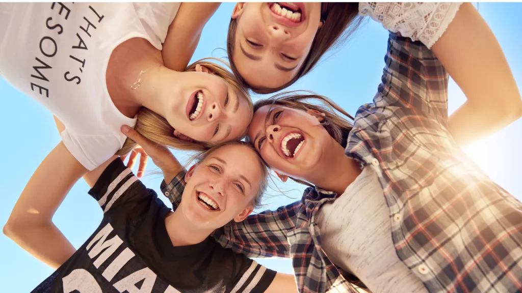 Four teenagers forming a circle while laughing and visiting a vacation spot for teens. 