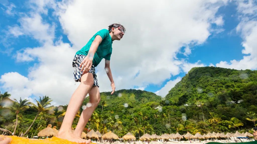 A water shot of a teen standing on a beach with the mountains as a backdrop. 