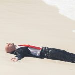 An image of a man in a business suit resting on a beach for an article about "work life balance."