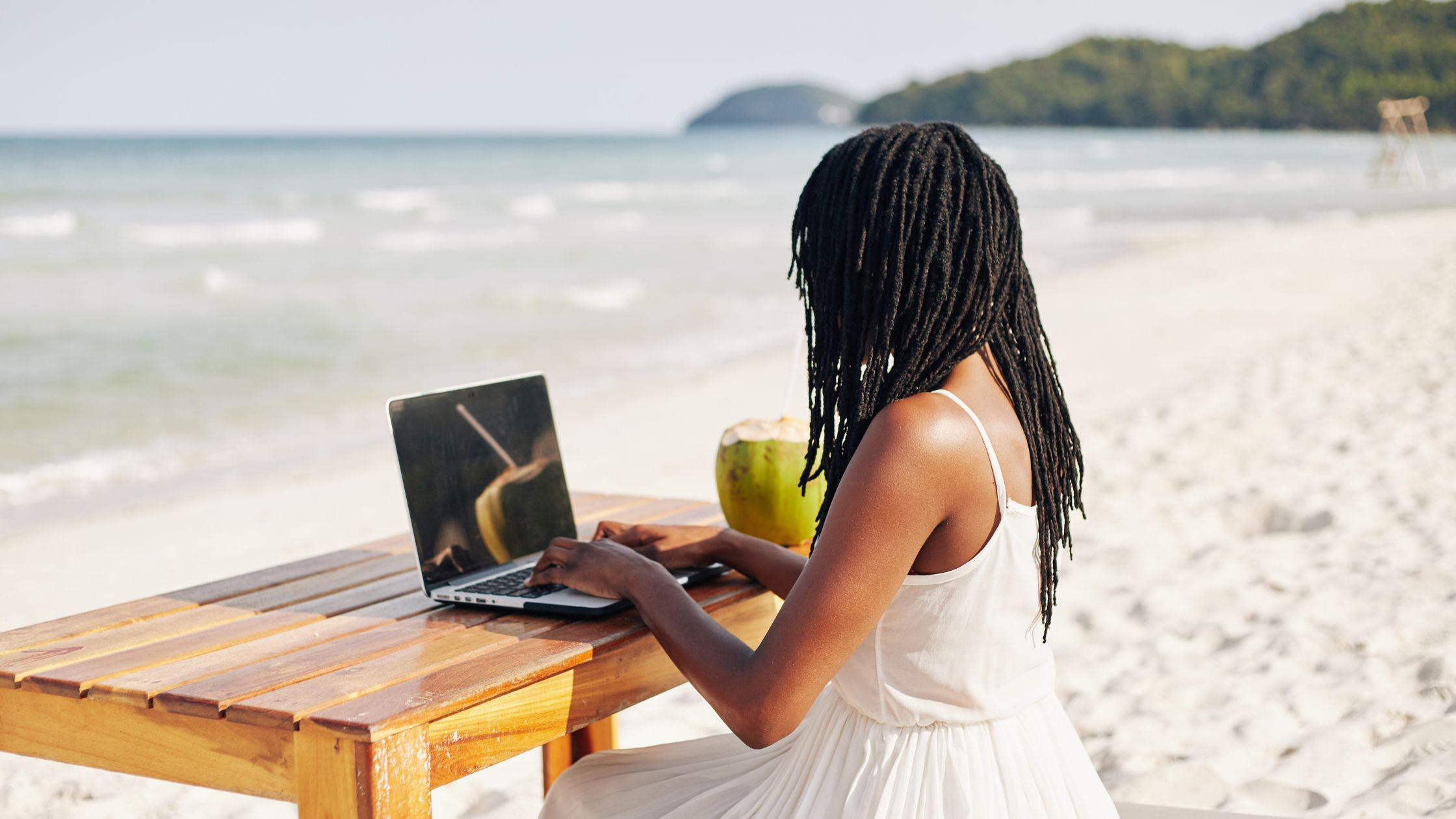 An image of a remote employee working at a beach for the article "does remote mean work from home?"