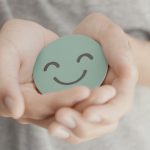 An image of a smiling emoji being held by a person for an article about "mental health for nomads."