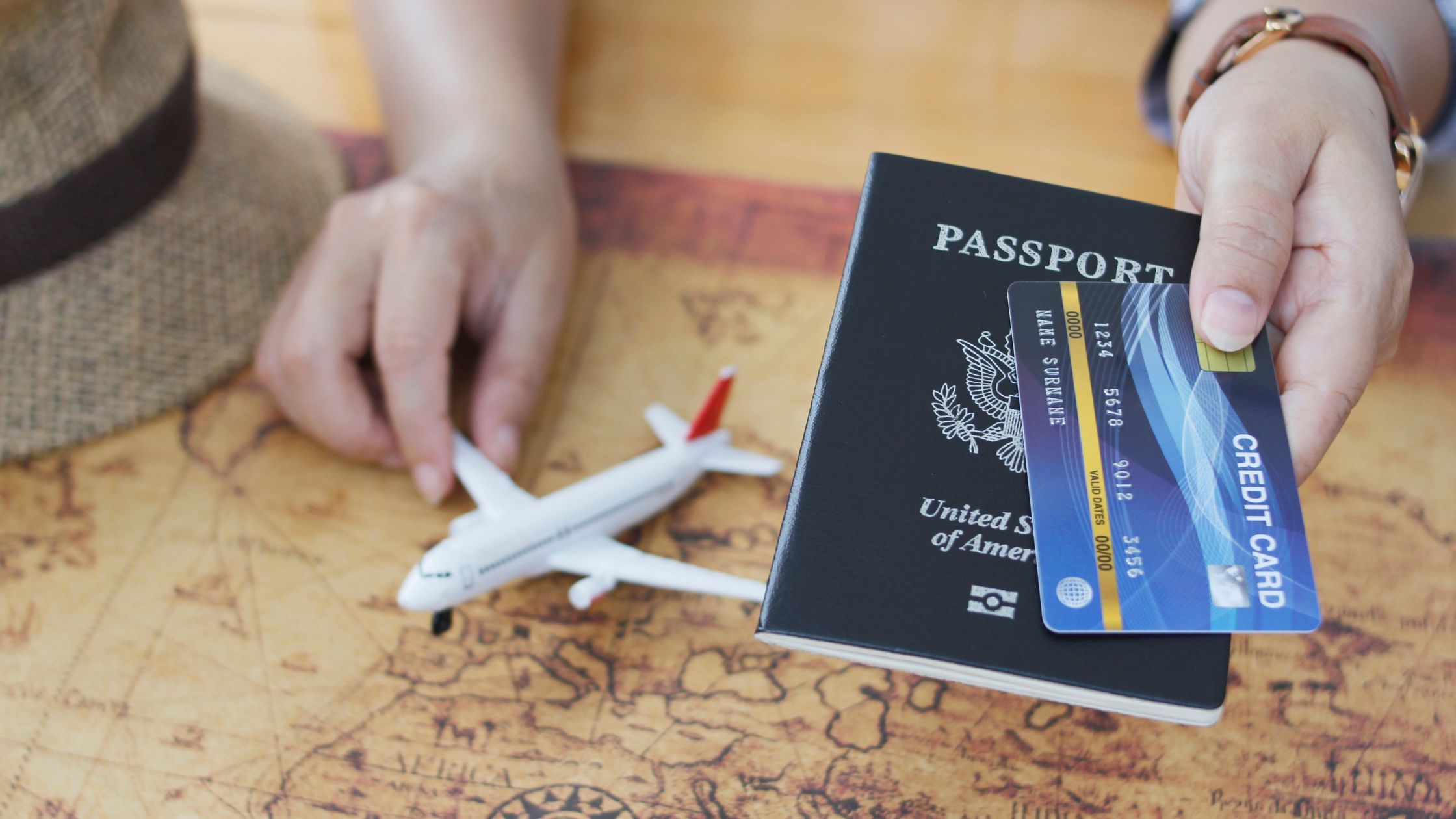An image of a person holding a toy plane, passport, and a credit card for an article about "how long does it take to improve credit score."
