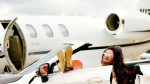 An image of a woman riding a luxury car with a private jet in the background for an article about "luxury travel on a budget."