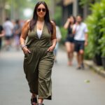 A woman in an olive jumpsuit walks confidently down a lively street, surrounded by people, representing the independence and freedom that multiple income streams can provide in a bustling, modern lifestyle.