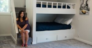 A woman sits by a built-in bunk bed in a neatly arranged, minimalist room, highlighting a cozy and inviting Airbnb setup. This image conveys the appeal of thoughtfully designed spaces in short-term rentals, addressing the question of whether the Airbnb dream is still achievable amidst changing industry trends in 2025.
