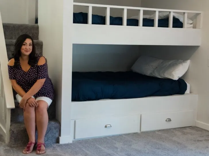 A woman sits by a built-in bunk bed in a neatly arranged, minimalist room, highlighting a cozy and inviting Airbnb setup. This image conveys the appeal of thoughtfully designed spaces in short-term rentals, addressing the question of whether the Airbnb dream is still achievable amidst changing industry trends in 2025.