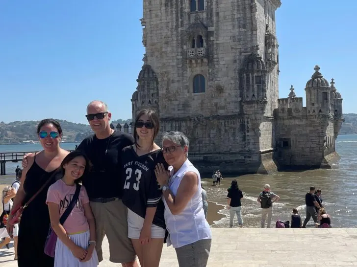 A smiling American family poses in front of the iconic Belém Tower in Lisbon, Portugal, showcasing their successful relocation journey. The sunny backdrop and historic architecture highlight the appeal of Portugal as a destination for expats seeking a fresh start. #AmericansMovingToPortugal