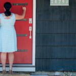 A woman in a polka-dot dress is seen from behind, knocking on a bright red front door with a smart lock installed, emphasizing secure and convenient entry. This image highlights the benefits of using a smart lock for easy and seamless Airbnb guest check-ins, eliminating the need for traditional keys and enhancing the guest experience.