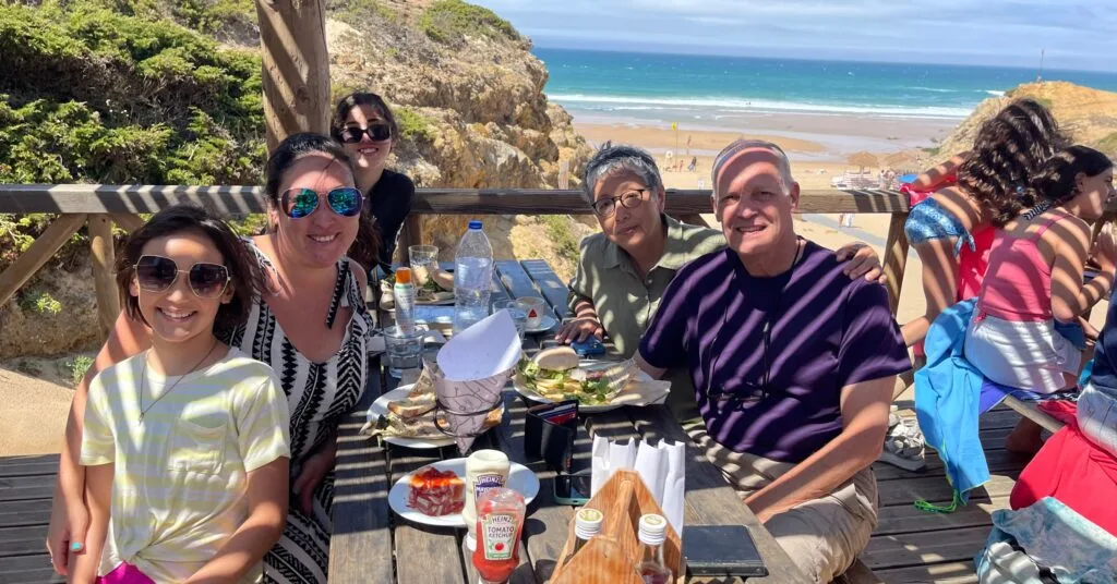 A family enjoying a sunny outdoor meal overlooking a stunning beach in Portugal. This snapshot captures the relaxed lifestyle many Americans seek when moving to Portugal for better quality of life and adventure. #AmericansMovingToPortugal