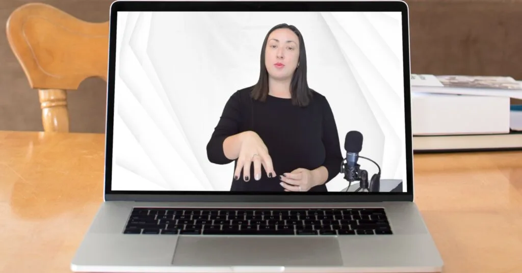 A laptop on a wooden table displays a video of a woman in a black top presenting confidently in front of a white background, with a microphone by her side, representing the potential to build authority and generate multiple income streams through online courses, webinars, and digital content creation.
