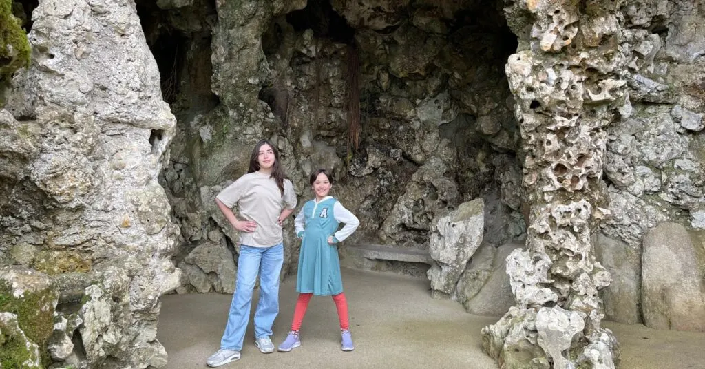 Two children pose confidently in front of a rocky grotto in Portugal, embracing their adventurous expat lifestyle. This vibrant moment showcases the enriching experiences for families when Americans move to Portugal. #AmericansMovingToPortugal