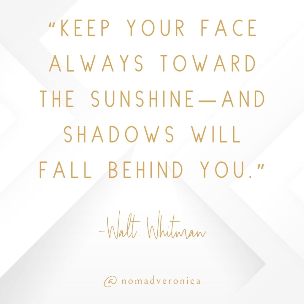 A motivational quote by Walt Whitman, "Keep your face always toward the sunshine—and shadows will fall behind you," is elegantly styled in gold text on a soft white geometric background. The design is subtly personalized with the handle "@nomadveronica," adding a touch of individuality to the inspiring message.