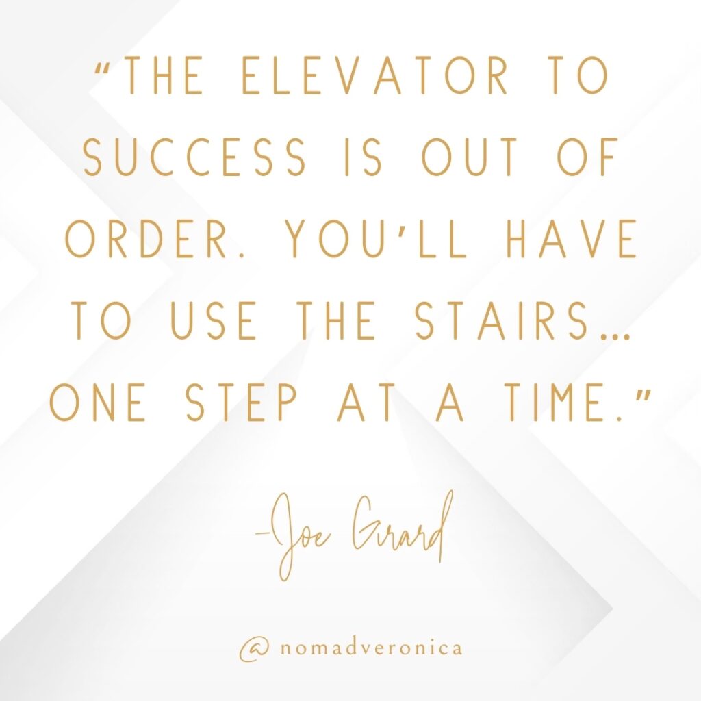 A motivational yet humorous quote by Joe Grand reads, "The elevator to success is out of order. You’ll have to use the stairs… one step at a time." This text is presented in gold lettering on a white geometric background, with the handle "@nomadveronica" included at the bottom. It humorously emphasizes perseverance and patience.