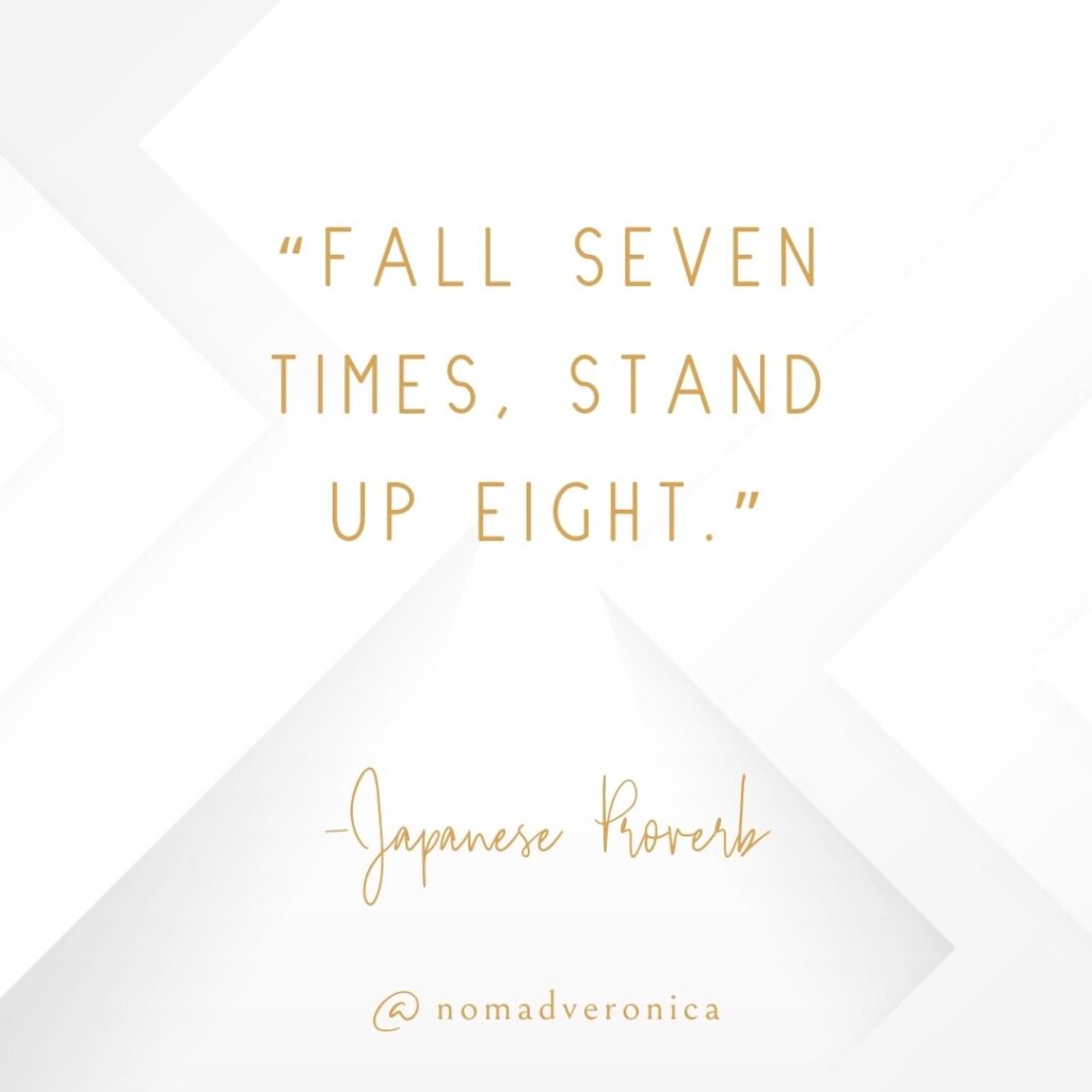 A minimalist design features the Japanese proverb, "Fall seven times, stand up eight," displayed in gold text on a clean, white geometric background. The quote is branded with the handle "@nomadveronica," offering an inspirational message of resilience and persistence.