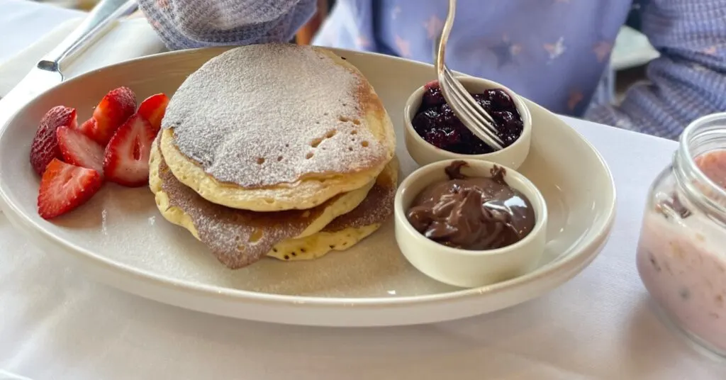 Delicious breakfast plate with fluffy pancakes, fresh strawberries, and side servings of jam and chocolate spread, showcasing the gourmet dining options at the best luxury hotels in Istanbul for families.