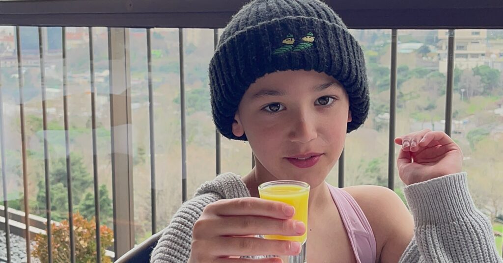 A child enjoying a glass of fresh orange juice on a balcony with a scenic view, highlighting the family-friendly amenities like complimentary breakfasts at the best luxury hotels in Istanbul.