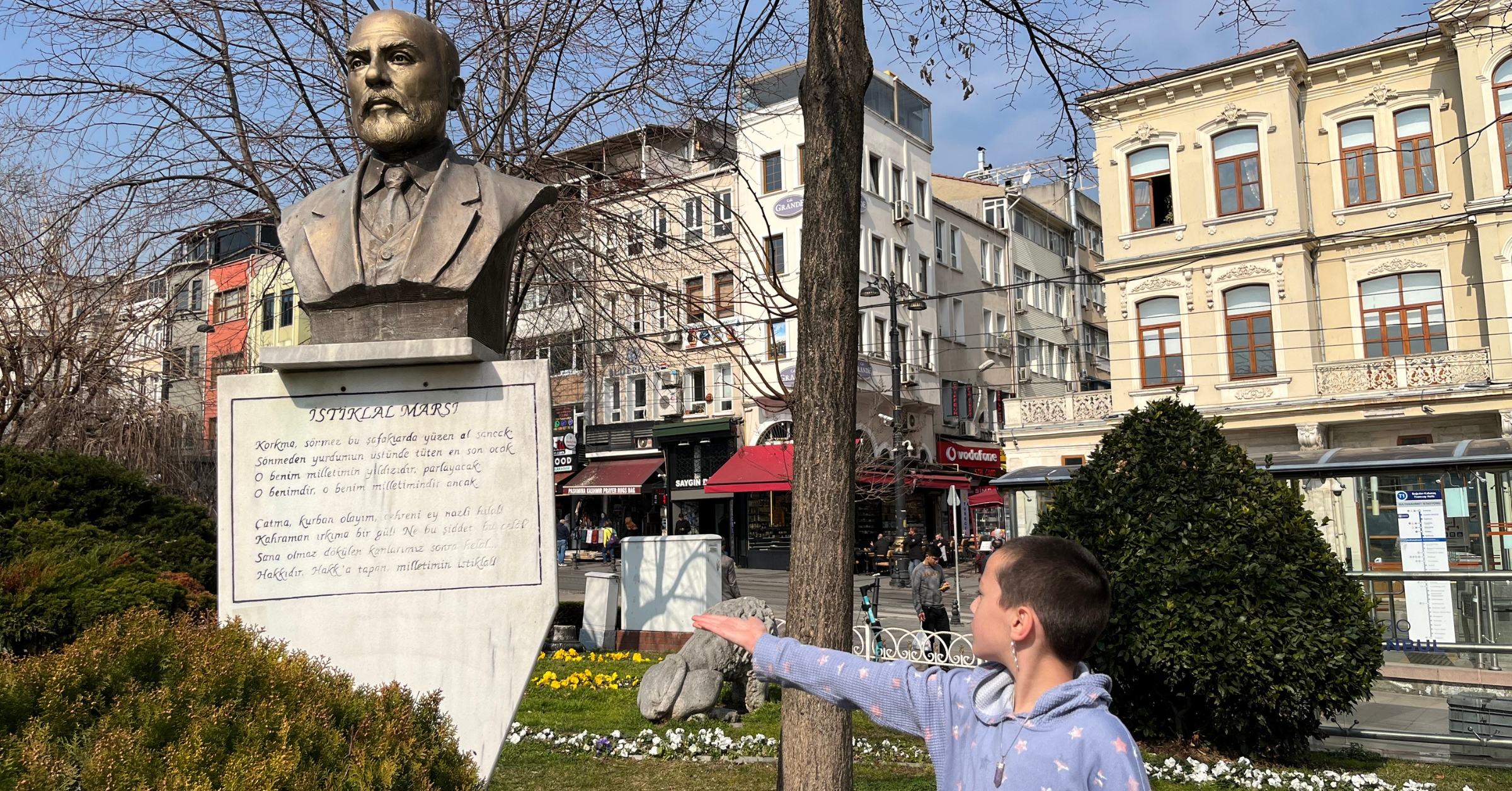 A child pointing at a statue of Mehmet Akif Ersoy in a public square in Istanbul, surrounded by historical buildings and gardens, showcasing educational and cultural things to do in Istanbul, Turkey, with kids.