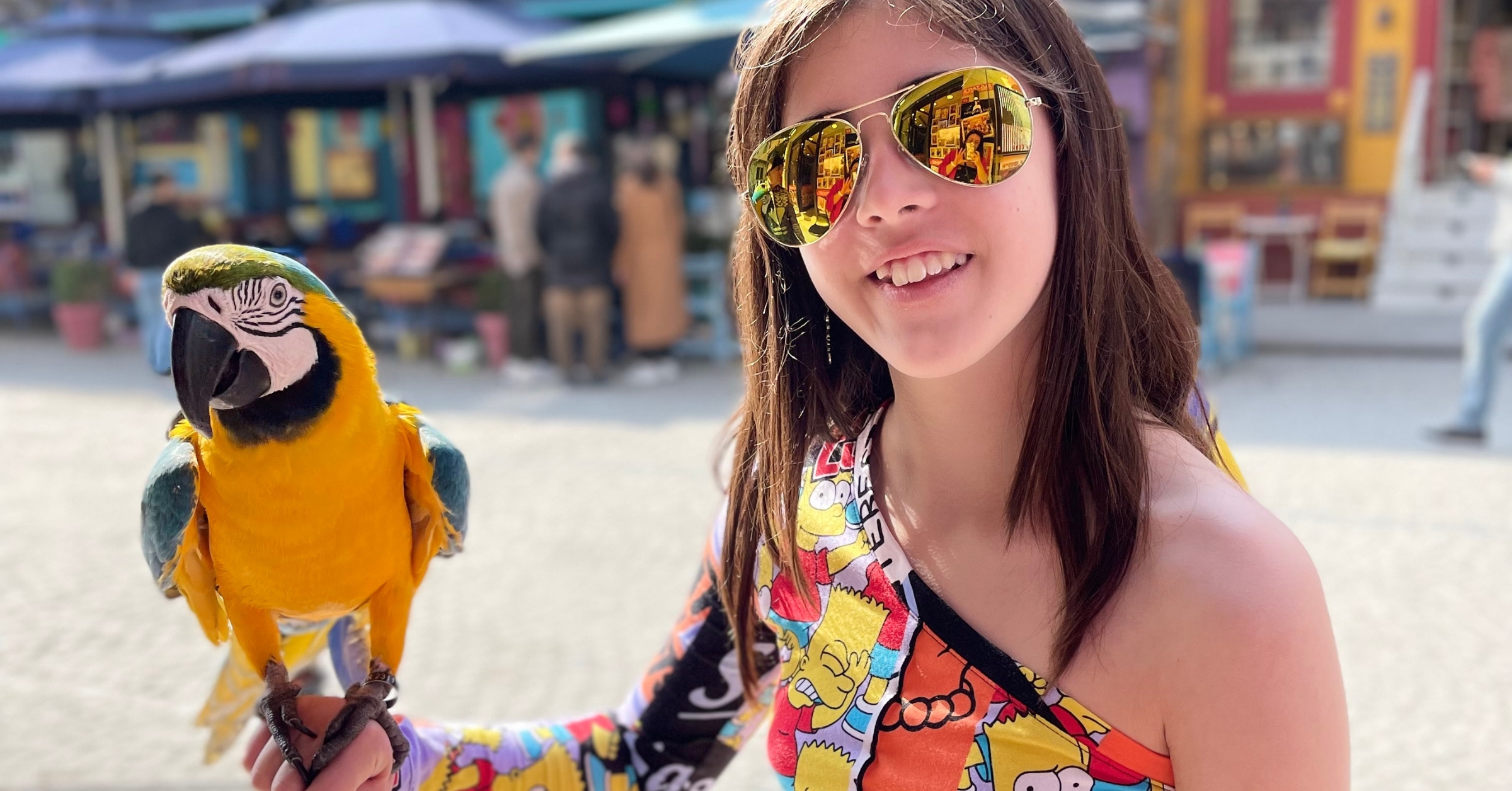 A smiling child holding a vibrant yellow-and-blue parrot at a colorful outdoor market in Istanbul. A unique and interactive experience, perfect for families exploring fun things to do in Istanbul with kids.