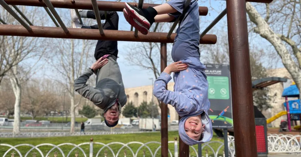 A father and daughter hanging upside down on a jungle gym at a playground in Istanbul, enjoying outdoor activities. A playful moment that highlights fun things to do in Istanbul with kids, perfect for family travel.