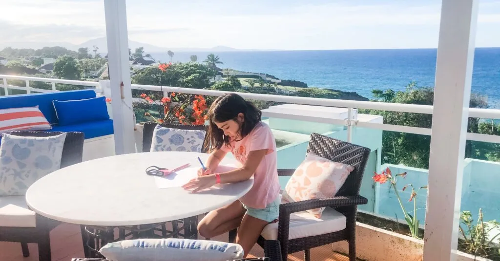 Young girl doing schoolwork on a breezy terrace with ocean views, showcasing a relaxed family lifestyle while living in Dominican Republic.