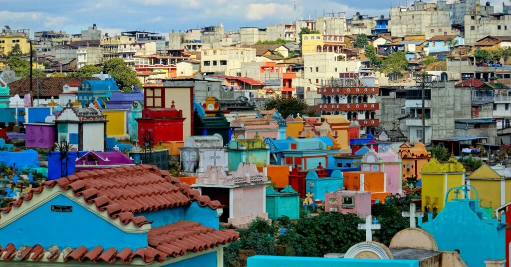 A vibrant cemetery in Guatemala with colorful tombs against a backdrop of a densely packed hillside city. A striking mix of culture and tradition, showcasing the unique approach to honoring ancestors in Guatemala.