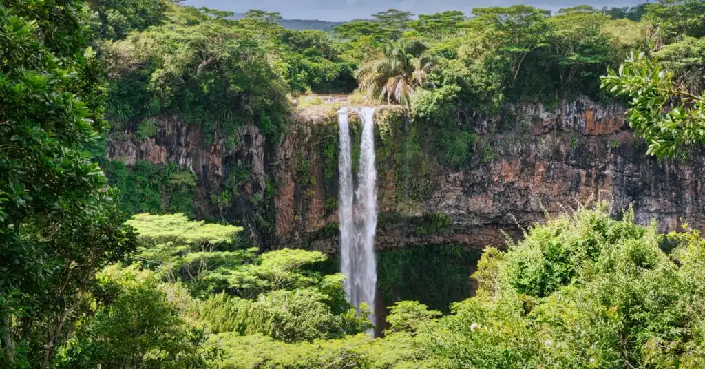 A stunning waterfall cascades down a rocky cliff, surrounded by dense tropical vegetation in Mauritius. A perfect glimpse into the island’s natural beauty for expats seeking adventure.