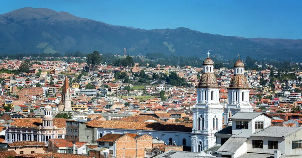 A panoramic view of Cuenca, Ecuador, showcasing colonial-style churches and red-roofed houses with the Andes mountains in the background. A favorite city among Ecuador expats for its charm and affordability.