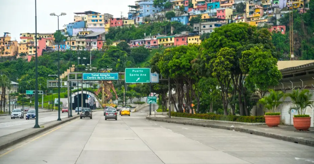 A busy road leading into Guayaquil, Ecuador, with colorful hillside homes and greenery in the background. This coastal city is a popular destination for Ecuador expats seeking a warmer climate.