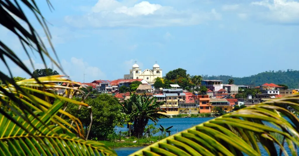A picturesque lakeside town in Guatemala framed by palm trees, with a historic church in the background. Many expats moving to Guatemala are drawn to charming, peaceful towns like this.
