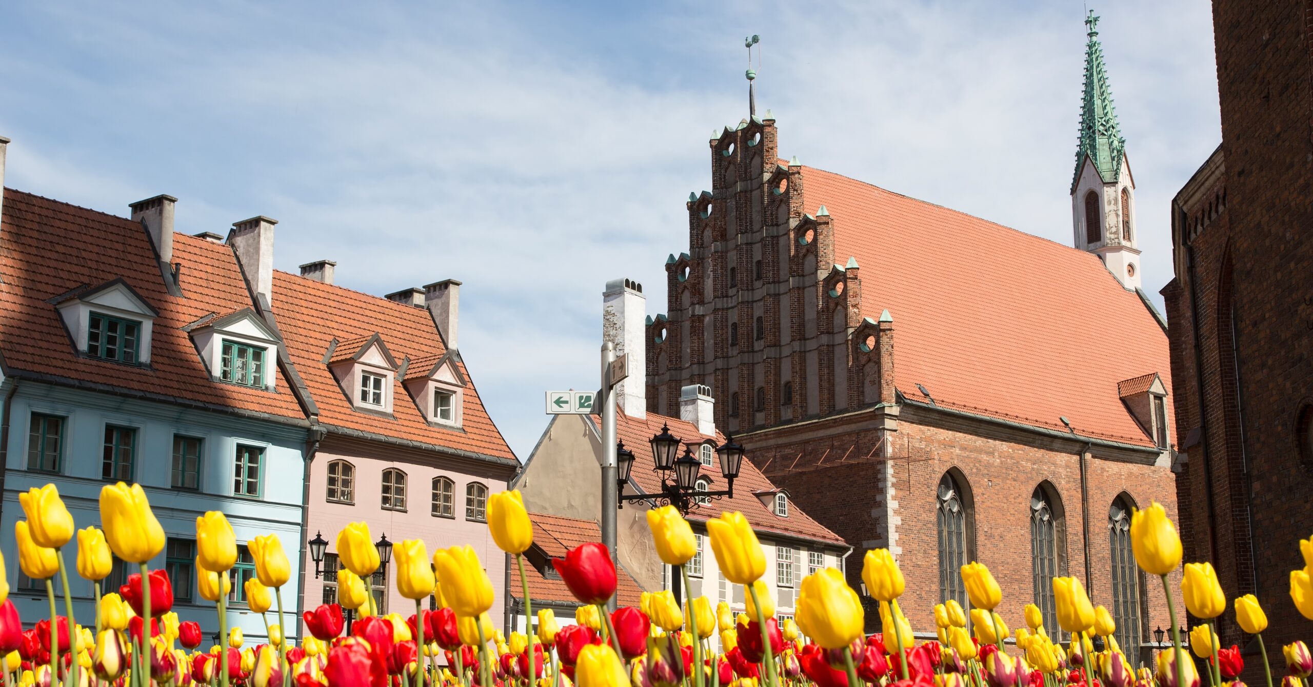 Vibrant red and yellow tulips bloom in front of historic brick and pastel-colored buildings in Riga, capturing the lively spring atmosphere of living in Latvia.