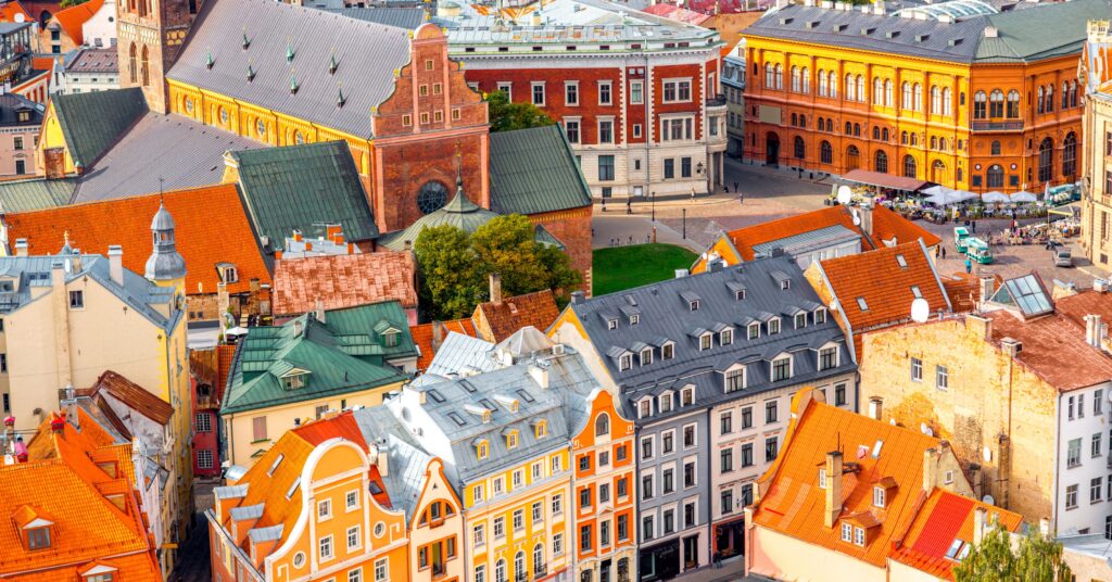 A high-angle view of Riga’s city center showing orange rooftops, historic churches, and public squares bustling with cafes — giving a sense of the vibrant city life that comes with living in Latvia.