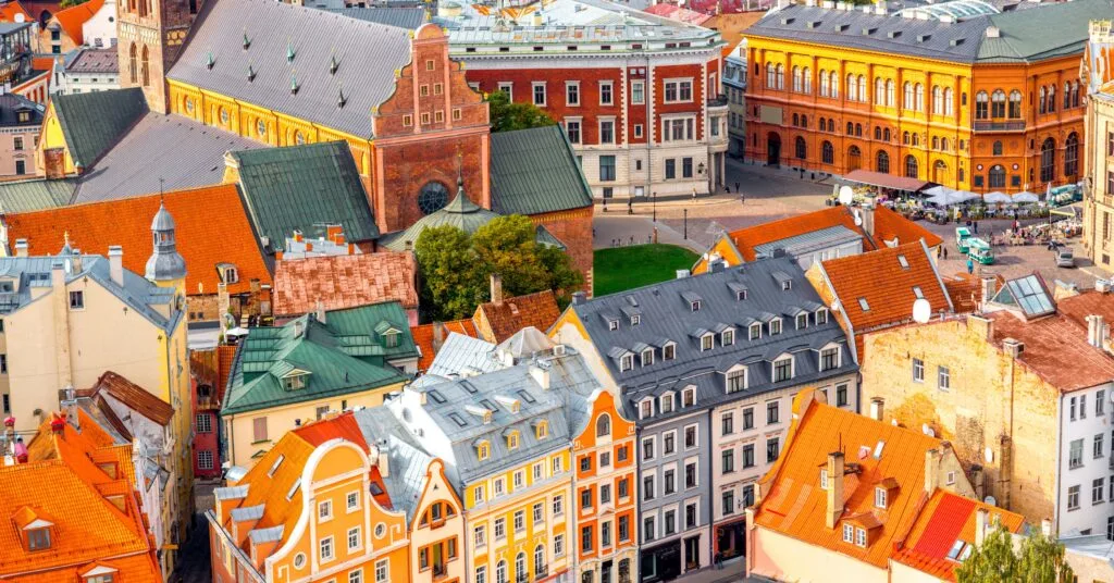 A high-angle view of Riga’s city center showing orange rooftops, historic churches, and public squares bustling with cafes — giving a sense of the vibrant city life that comes with living in Latvia.