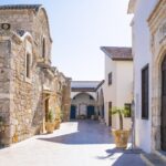A peaceful courtyard surrounded by stone buildings with arched entrances and potted palm trees. The architectural beauty of Cyprus is a major attraction for expats.