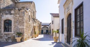A peaceful courtyard surrounded by stone buildings with arched entrances and potted palm trees. The architectural beauty of Cyprus is a major attraction for expats.