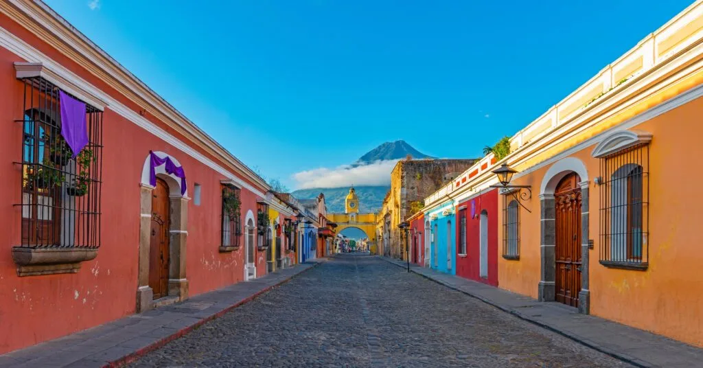 A scenic street in Antigua, Guatemala, featuring vibrant colonial architecture and a towering volcano in the distance. A top destination for expats moving to Guatemala who love history and charm.