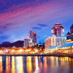 A dazzling view of the Port Louis waterfront lit up at night, with modern buildings reflecting on the calm waters. Mauritius offers expats a vibrant nightlife and shopping scene.