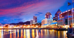 A dazzling view of the Port Louis waterfront lit up at night, with modern buildings reflecting on the calm waters. Mauritius offers expats a vibrant nightlife and shopping scene.