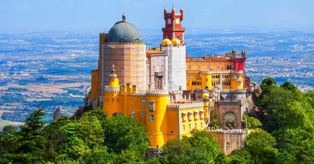 The vibrant and whimsical Pena Palace sits atop a lush green hill, overlooking the Portuguese countryside. If you’re thinking of moving to Portugal, this fairytale-like landscape awaits.