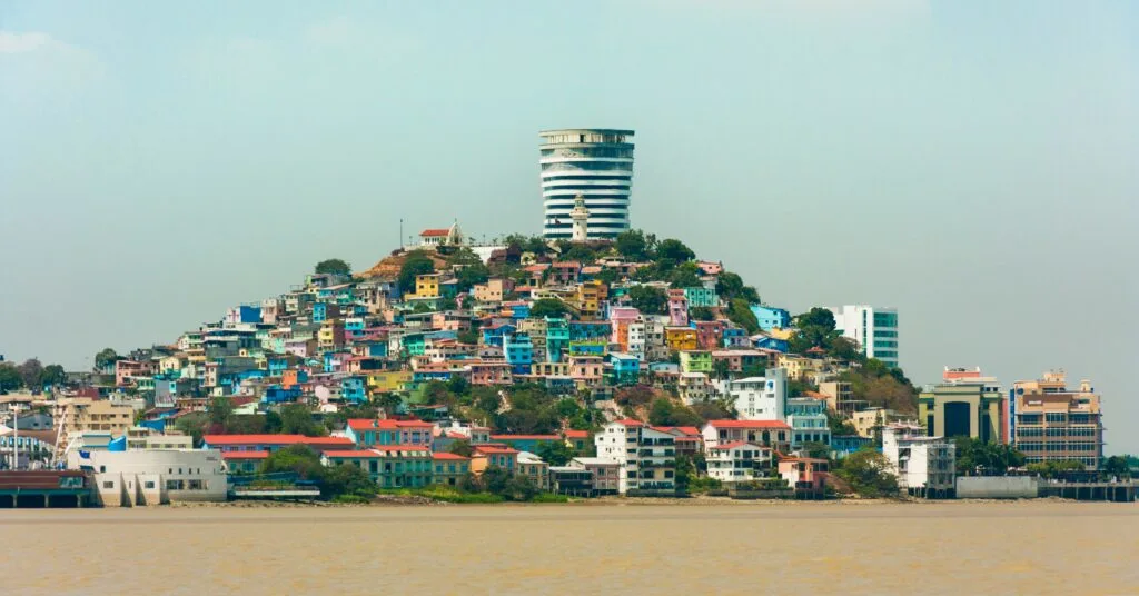 A vibrant hill covered in colorful houses in Guayaquil, Ecuador, featuring a historic lighthouse and modern high-rise in the background. A well-known spot among Ecuador expats.