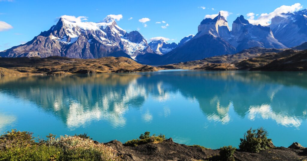 Stunning view of snow-capped mountains reflected in the turquoise waters of a lake in Torres del Paine National Park, showcasing Chile's natural beauty and appeal to nature-loving expats.