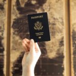 Person’s hand holding a U.S. passport in front of a sepia-toned world map backdrop, evoking preparation and excitement for exploring the cheapest countries to move to from America.