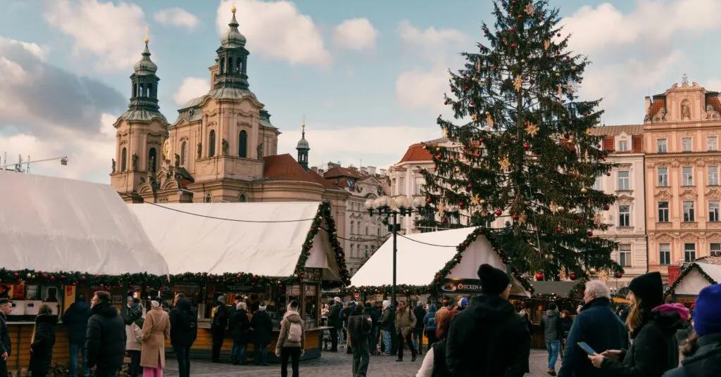 Crowds browse festive stalls at a European Christmas market decorated with garlands and a large tree, showcasing cultural richness in some of the cheapest countries to move that still offer seasonal magic.
